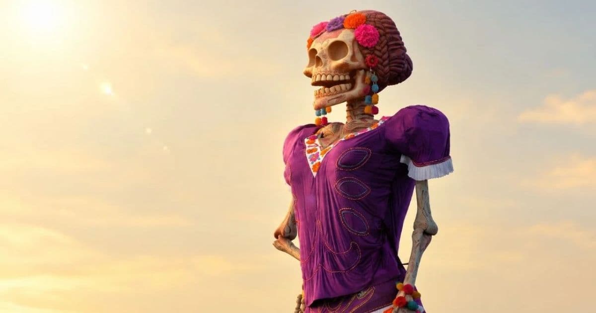 Catrina monumental con vestido morado, calavera decorada y flores de colores ante un cielo al atardecer