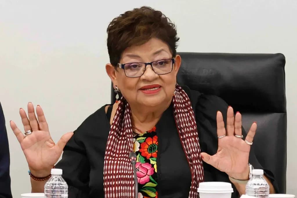 Ernestina Godoy sentada frente a un micrófono, con ambas manos levantadas y una bufanda roja y blanca