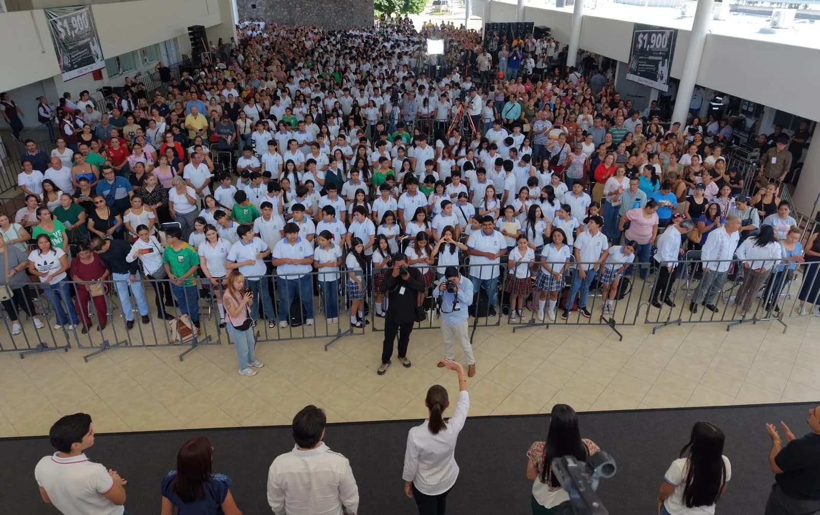 Vista elevada de estudiantes y otros asistentes reunidos frente a un escenario en un recinto amplio de Colima