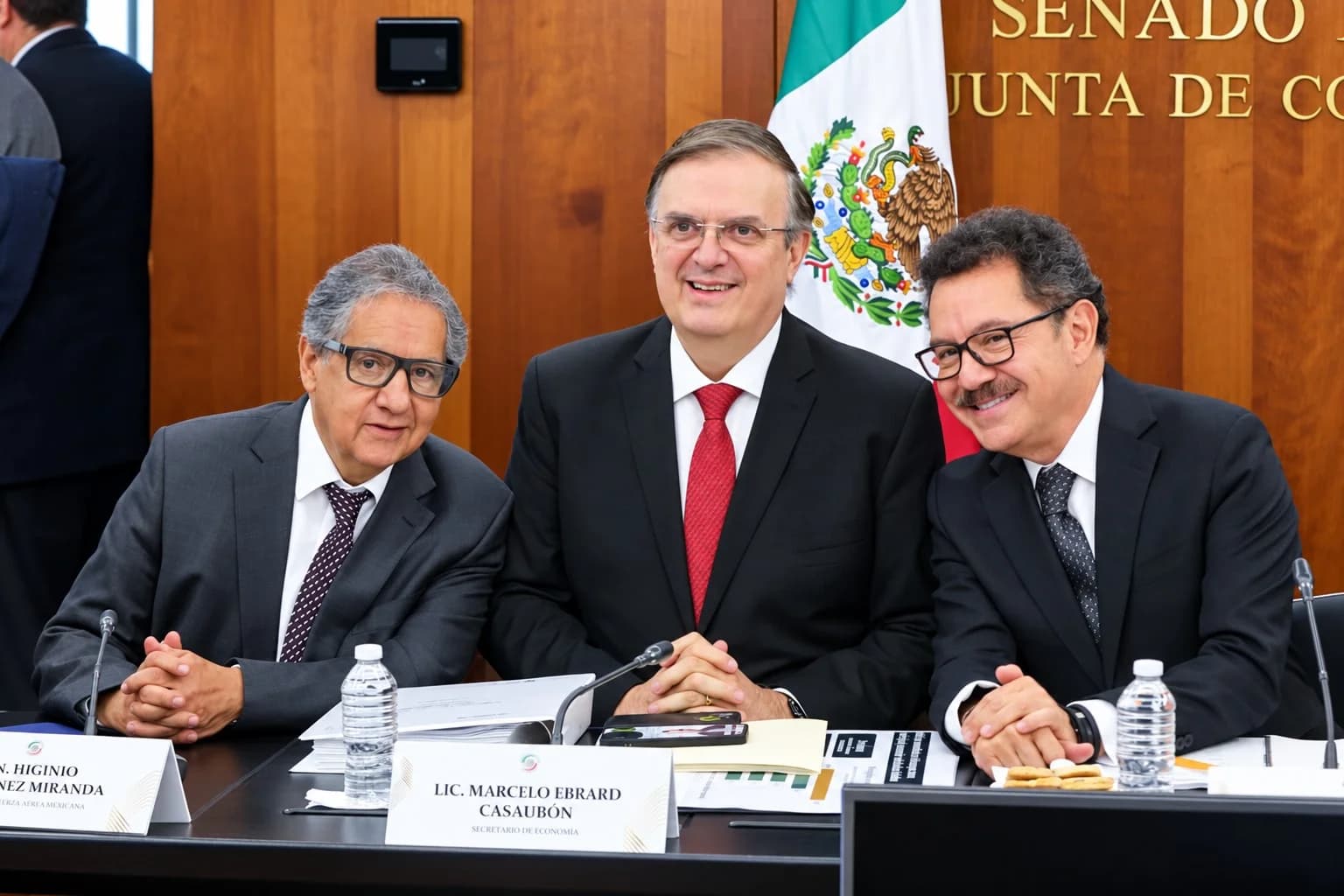 Tres funcionarios sentados a una mesa en una sala del Senado; Marcelo Ebrard aparece en el centro junto a la bandera de México