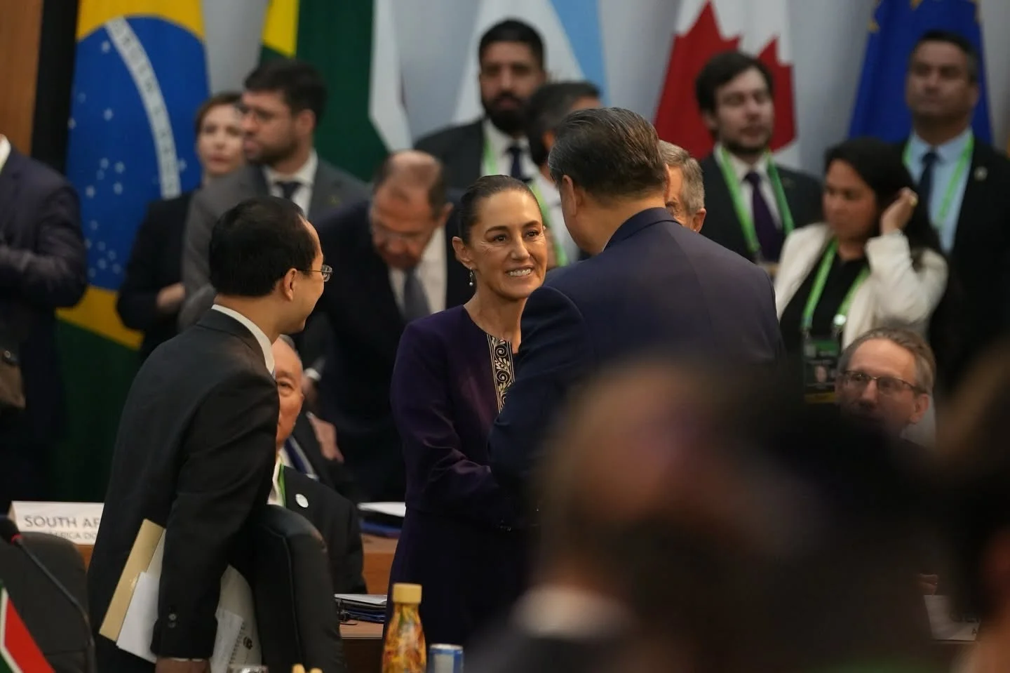 Claudia Sheinbaum conversa con Xi Jinping en una reunión internacional, rodeados de asistentes y representantes diplomáticos
