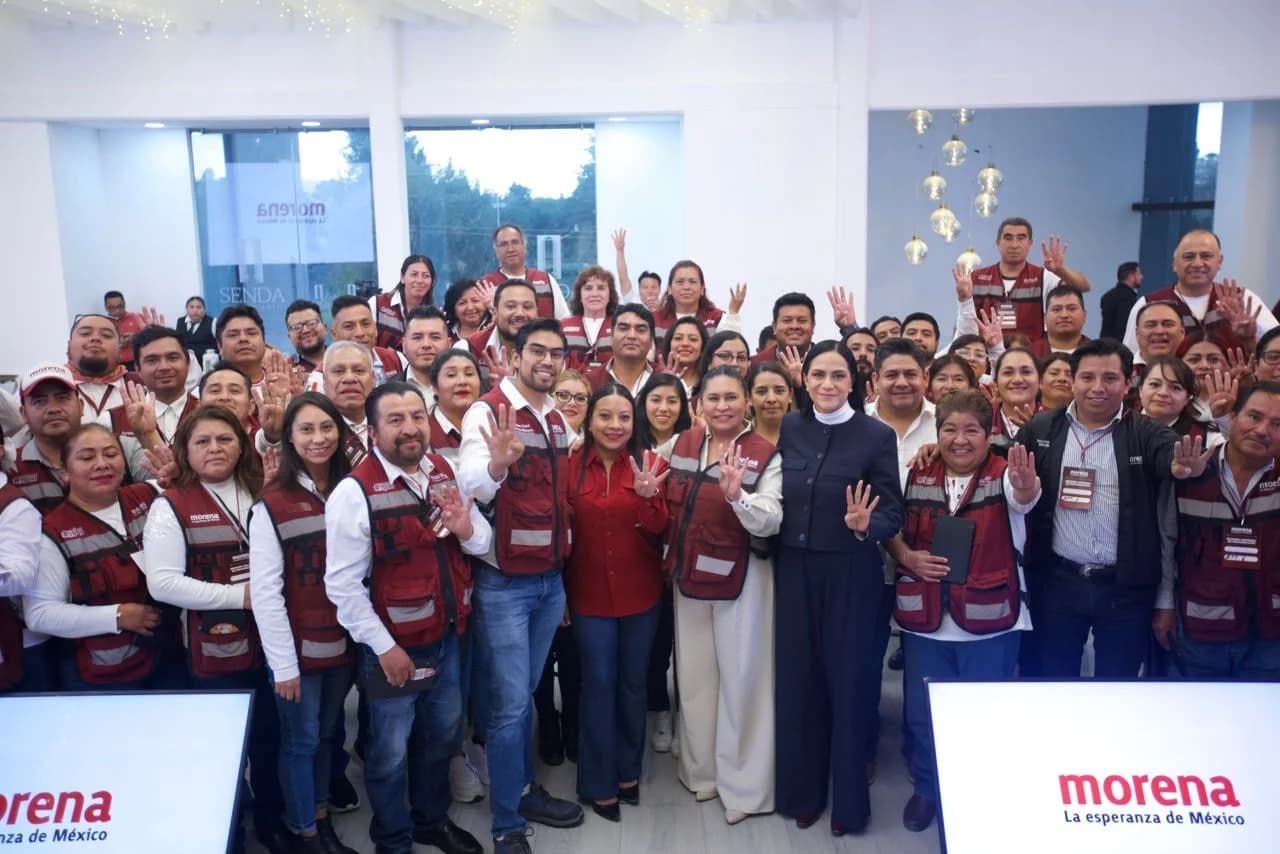 Integrantes de Morena posan para una fotografía grupal en un espacio interior, algunos con chalecos guinda del partido y las manos levantadas
