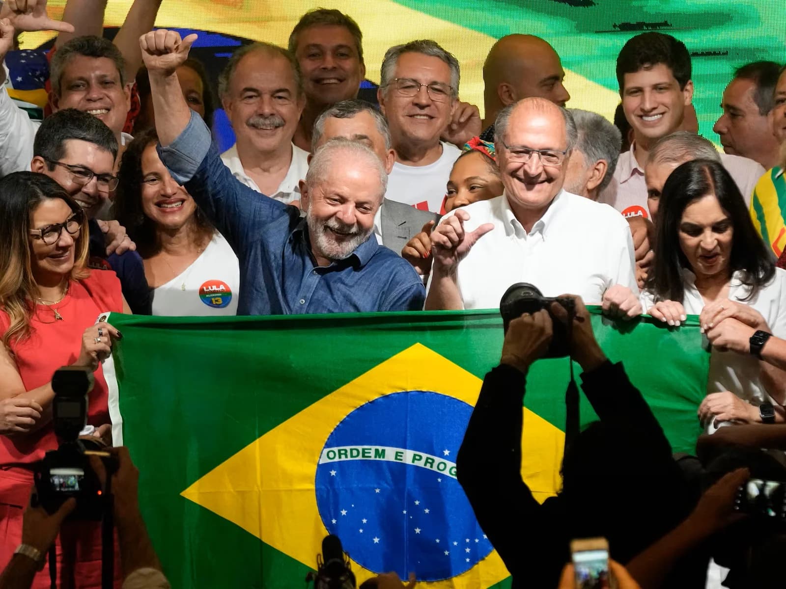 Lula da Silva levanta el brazo frente a seguidores con una bandera de Brasil en una celebración política.
