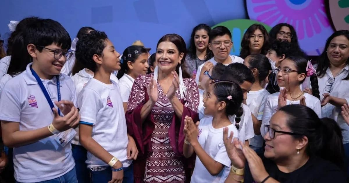 Clara Brugada rodeada de niñas, niños y adultos que aplauden en un escenario.