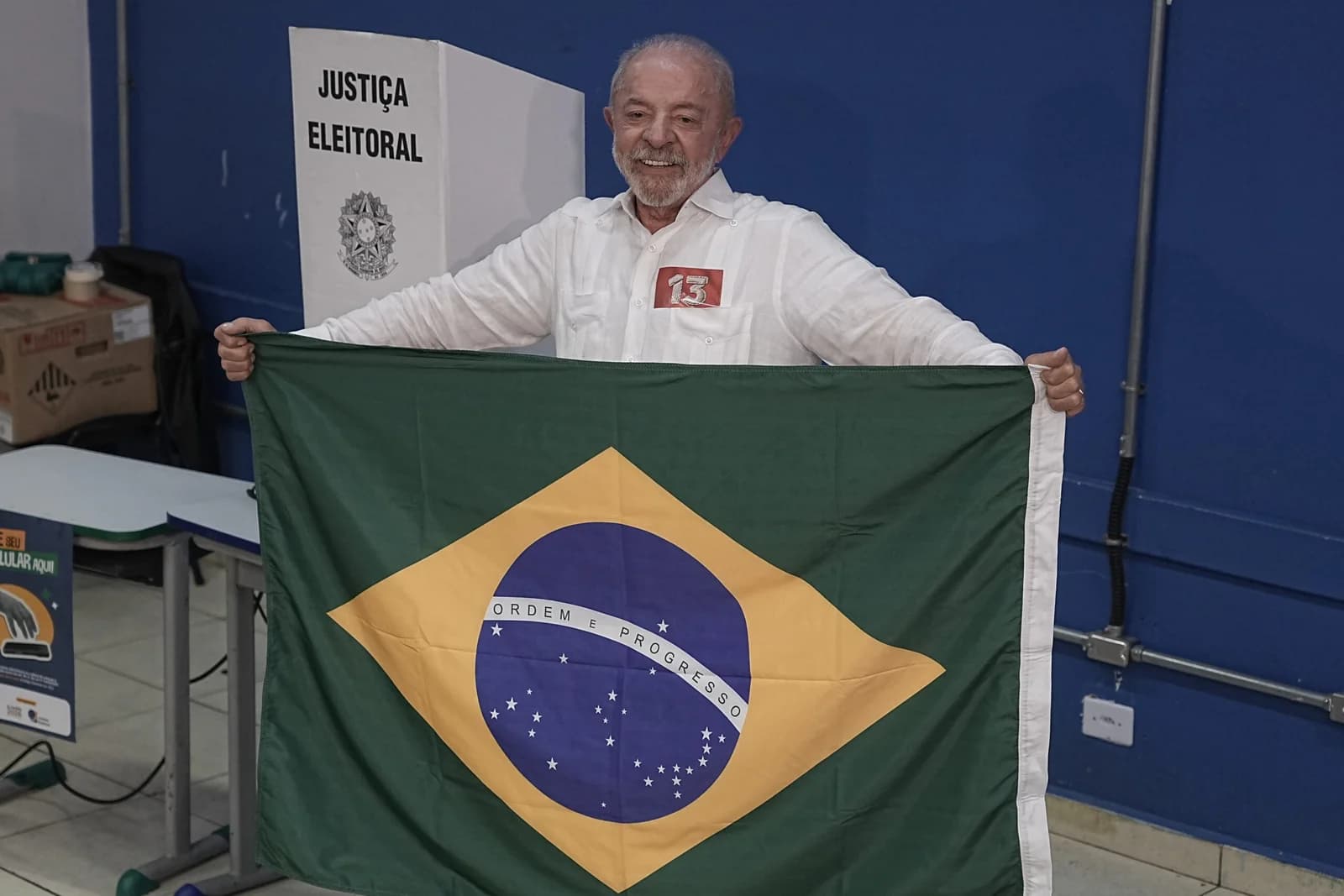 Luiz Inácio Lula da Silva sonríe mientras sostiene una bandera de Brasil frente a una mampara de justicia electoral