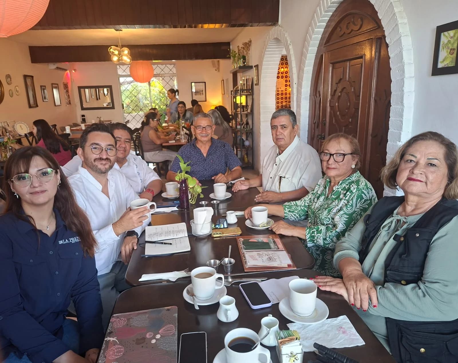 Grupo de siete personas sentado alrededor de una mesa en una cafetería, mirando a la cámara