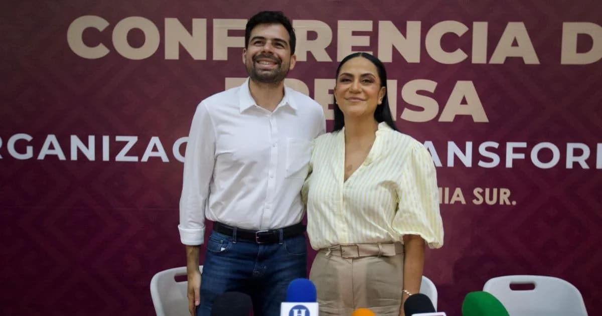 Dos personas de pie ante un fondo guinda en una conferencia de prensa.