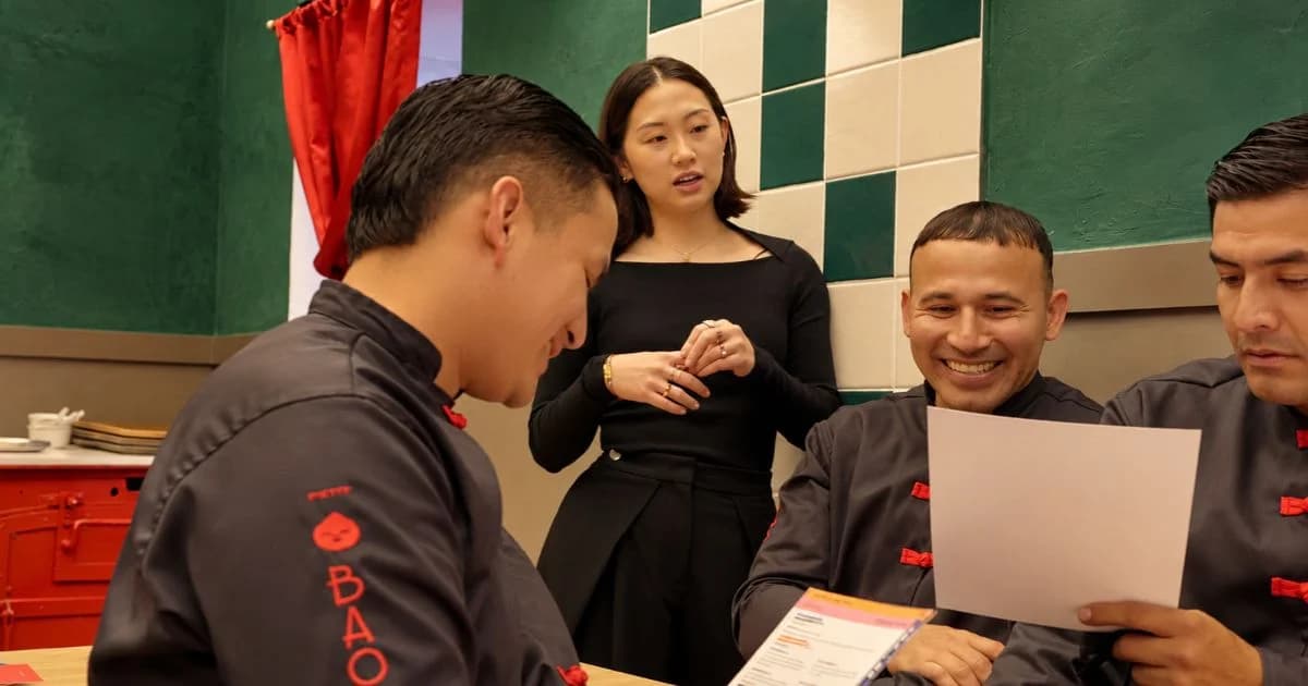Cuatro personas conversan y revisan menús en el interior de Petit Bao, con paredes verdes y detalles rojos