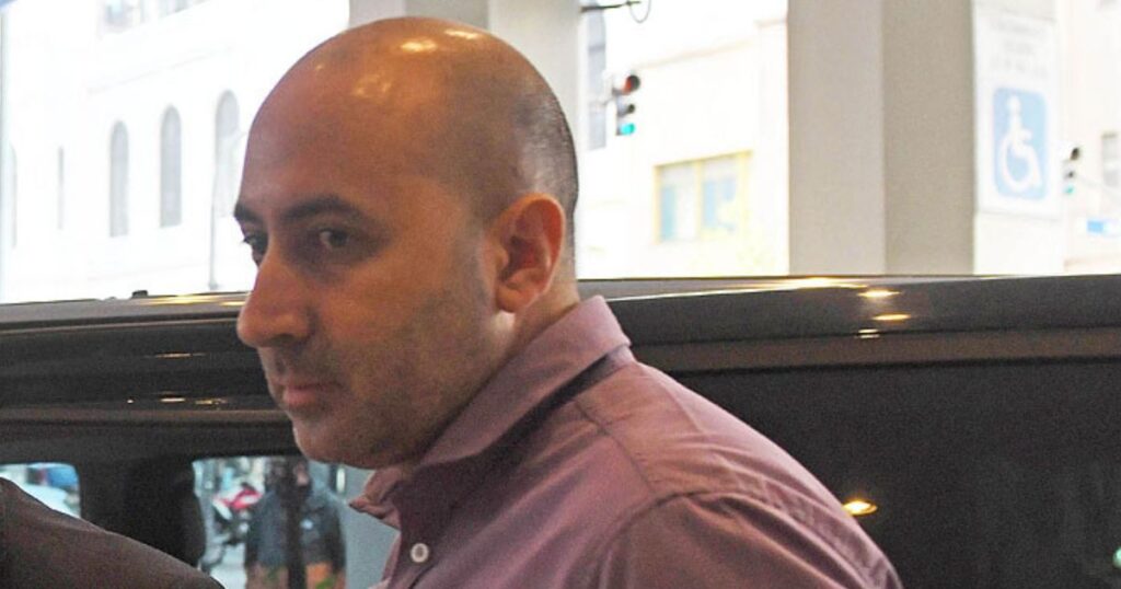 Fernando Cerimedo con camisa rosa junto a un vehículo en un espacio público