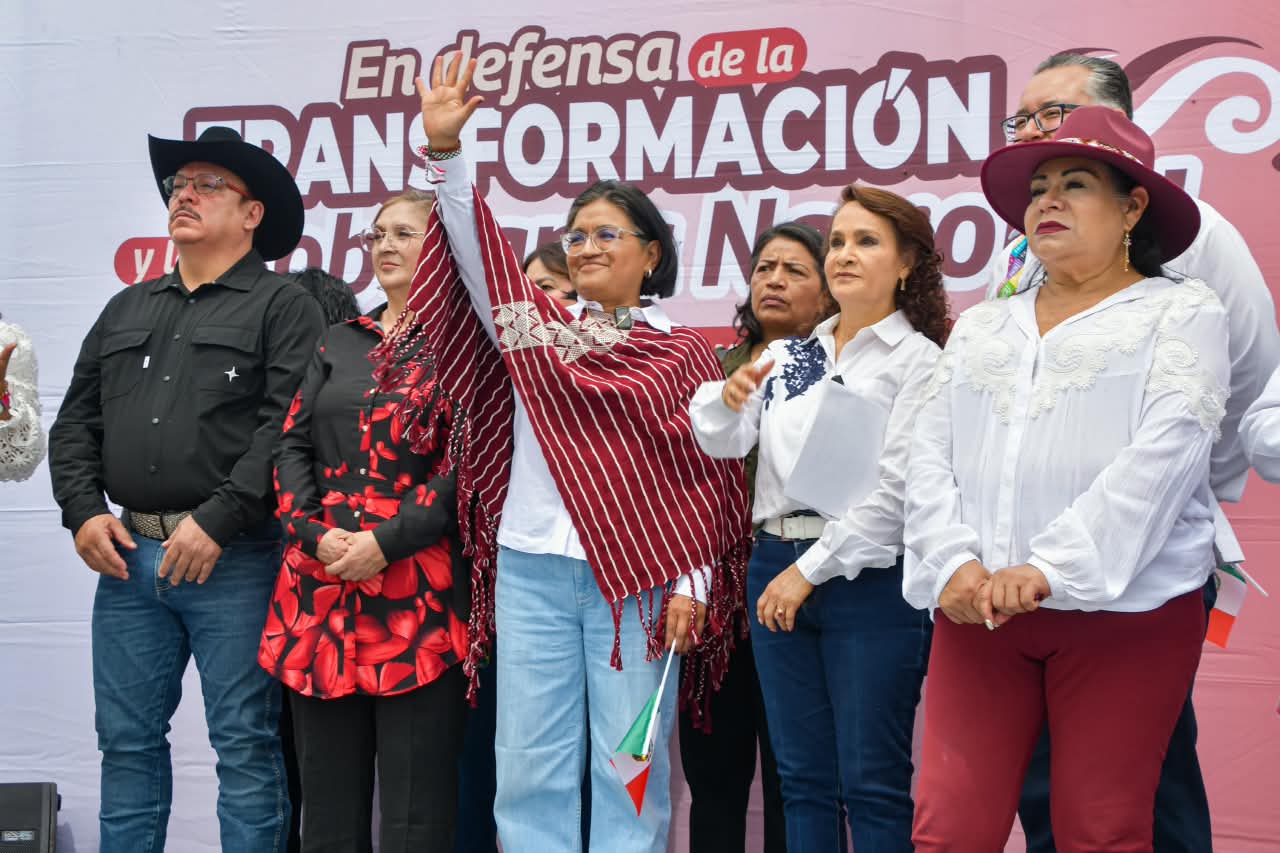 Personas participan en una asamblea por la defensa de la soberanía nacional, frente a un escenario con mensajes sobre la transformación.
