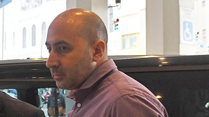 Fernando Cerimedo con camisa rosa junto a un vehículo en un espacio público