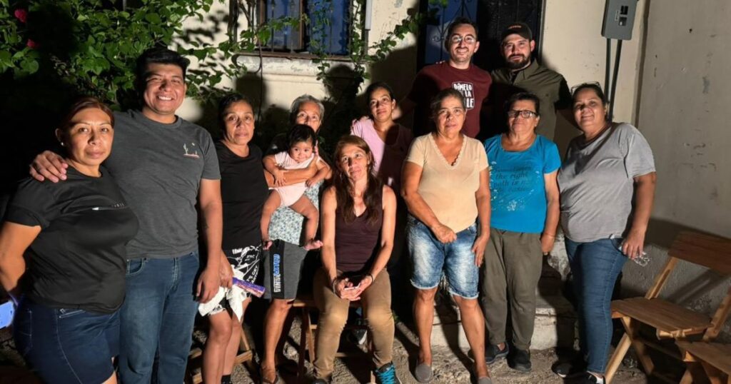 Grupo de vecinos y participantes durante una reunión nocturna en la colonia Olachea de La Paz, acompañados por un bebé y un perro