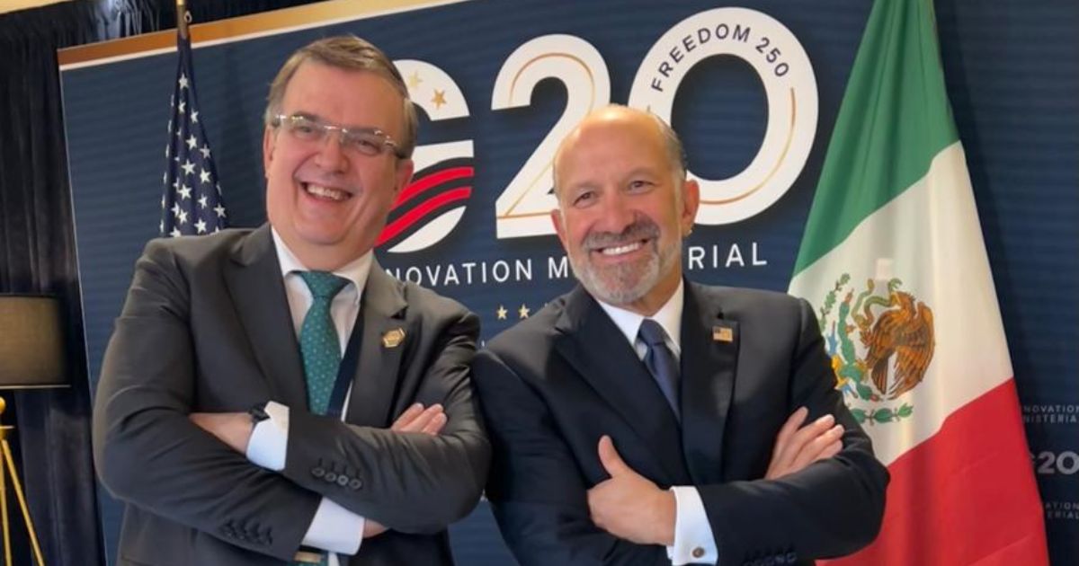 Marcelo Ebrard y Howard Lutnick posan sonrientes frente a las banderas de México y Estados Unidos durante un encuentro institucional en el G20