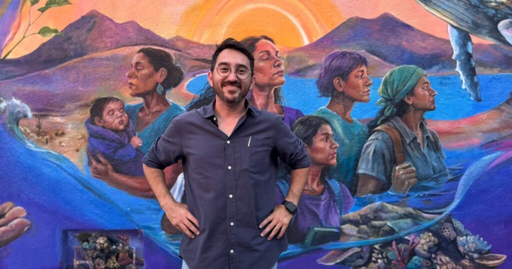 Frank Aguirre frente a un mural comunitario dedicado a los derechos humanos y la vida digna
