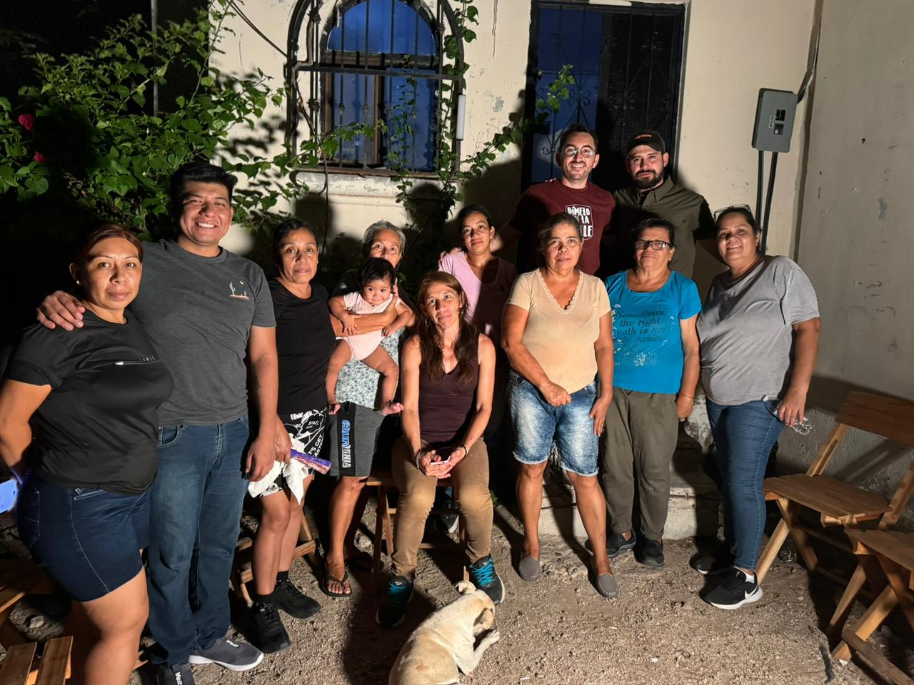 Grupo de vecinos y participantes durante una reunión nocturna en la colonia Olachea de La Paz, acompañados por un bebé y un perro