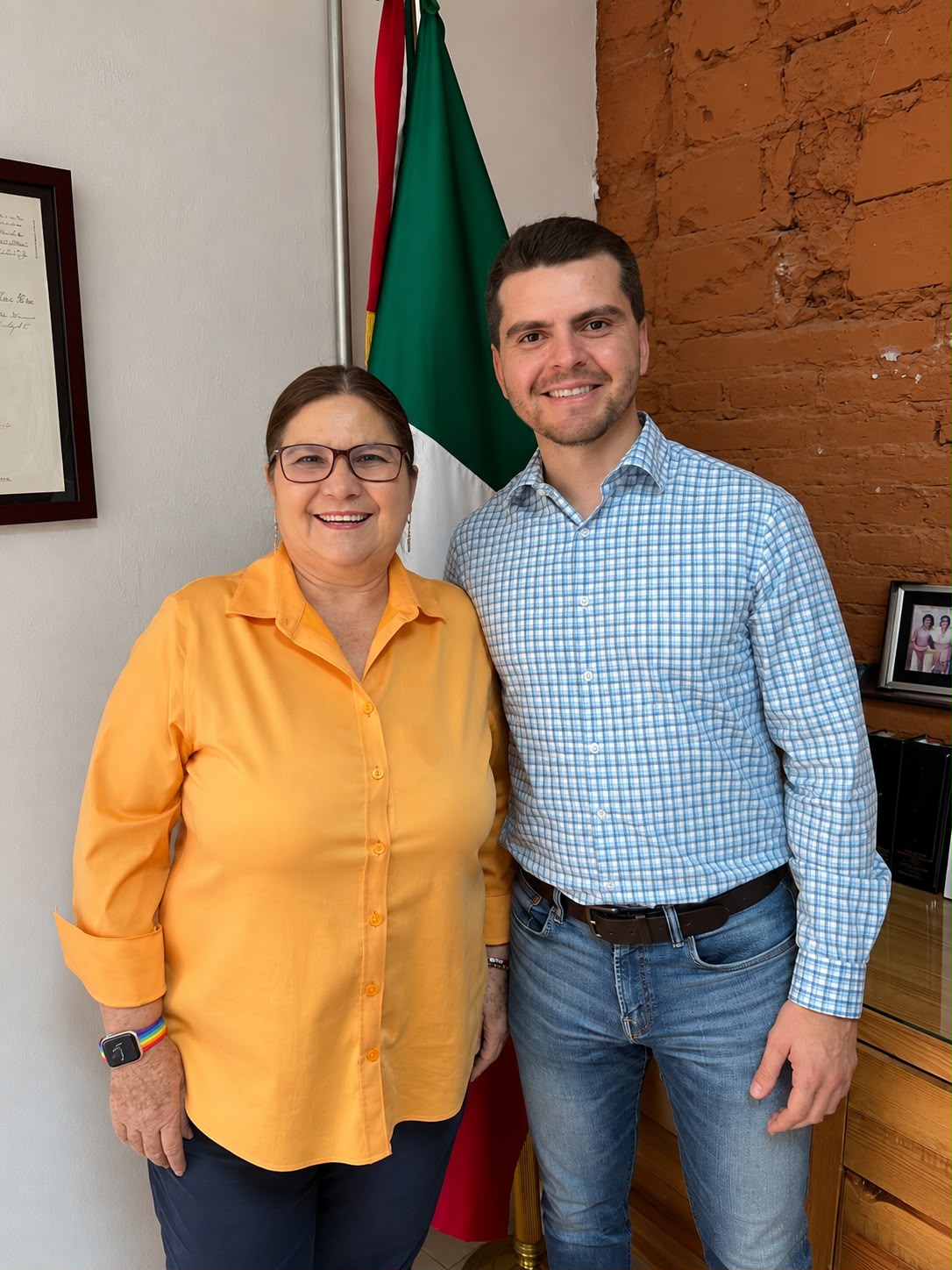 Alonso Ramíez e Imelda Castro posan de pie frente a una bandera de México en una oficina