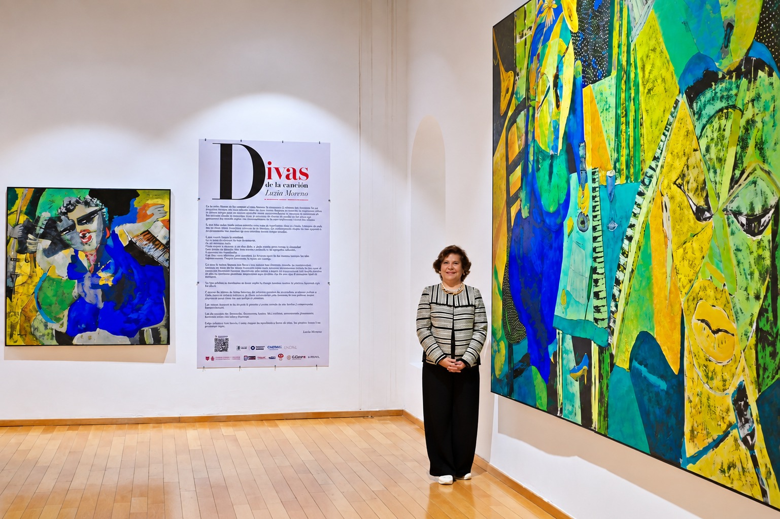 Artista posa en una sala de exposición entre pinturas de gran formato y el cartel de Divas de la canción