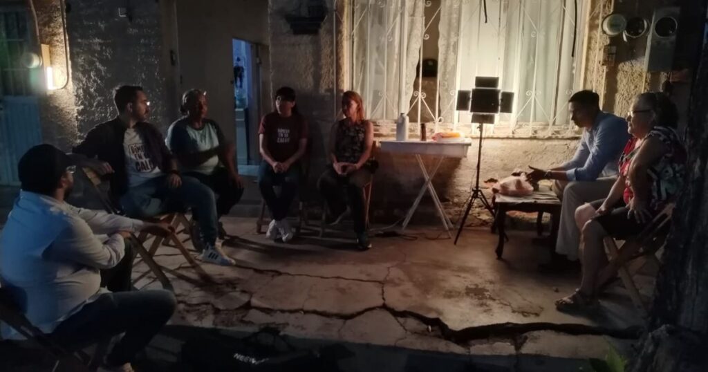 Varias personas participan en una reunión vecinal nocturna en el exterior de una vivienda.
