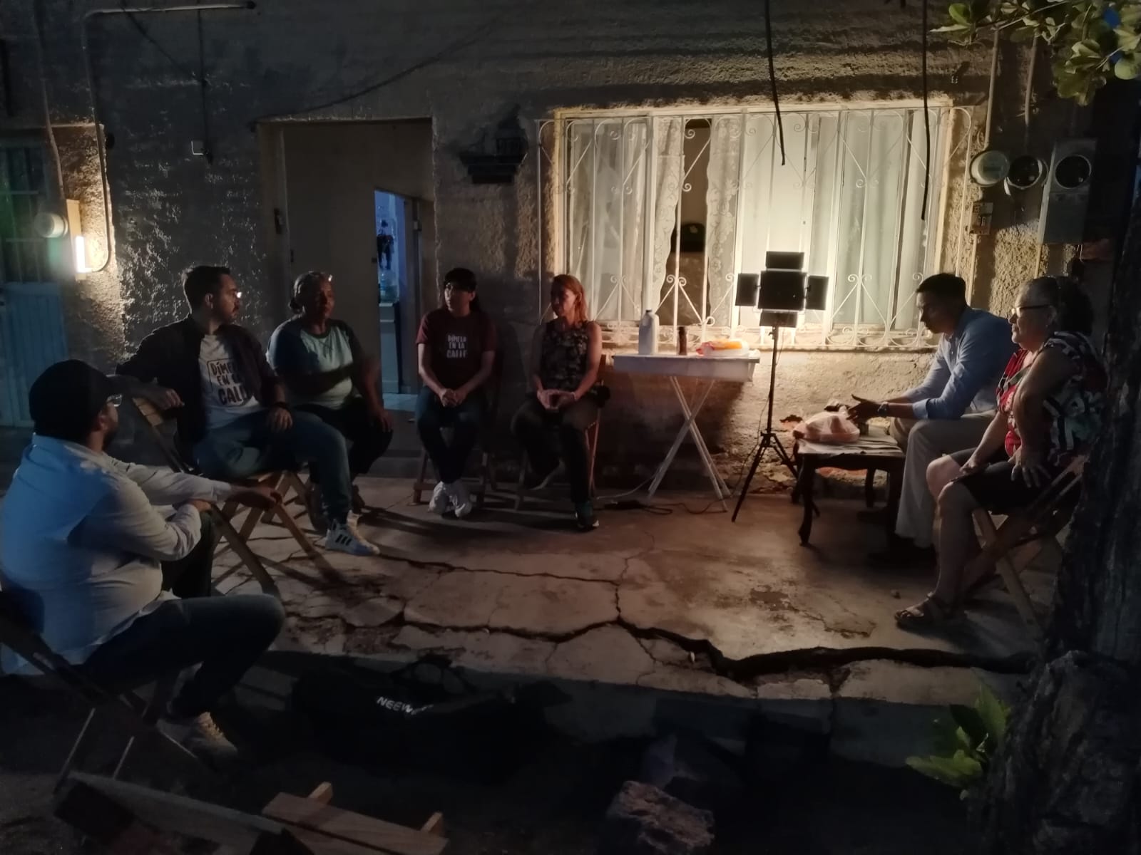 Varias personas participan en una reunión vecinal nocturna en el exterior de una vivienda.