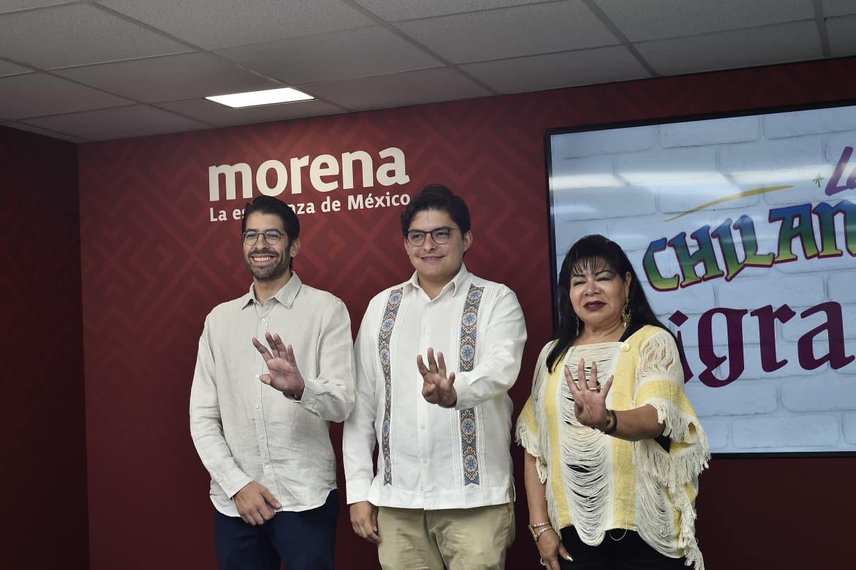 Tres personas posan frente a un muro con el logotipo de Morena