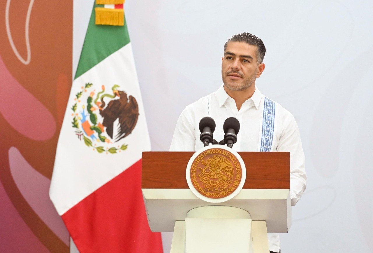 Funcionario federal durante una conferencia sobre seguridad en Chiapas, frente a la bandera de México