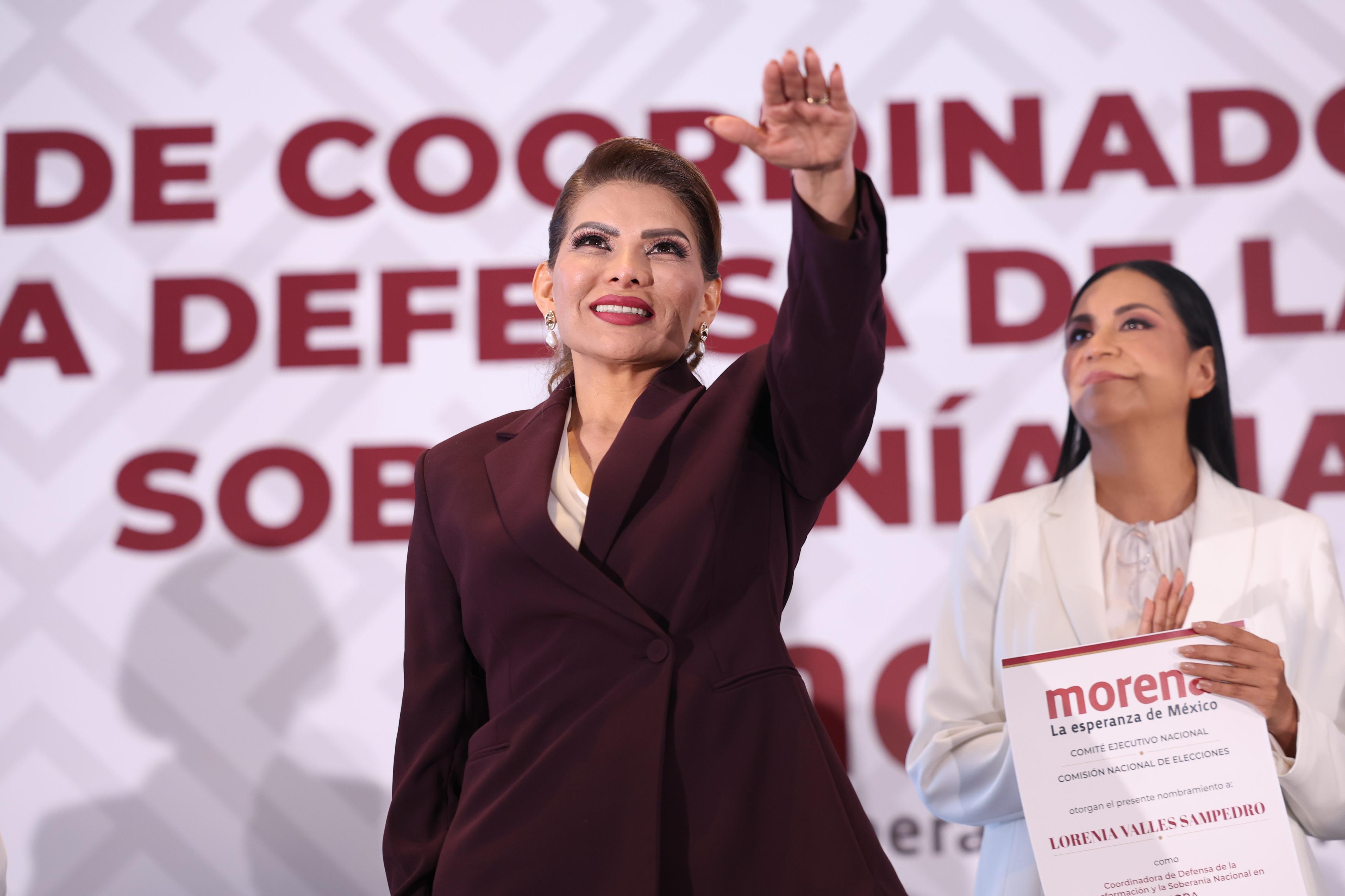 Mujer levanta la mano durante un acto político mientras otra persona sostiene un nombramiento de Morena