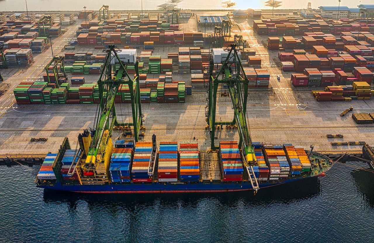 Vista aérea de grúas portuarias junto a un buque cargado de contenedores y una terminal de carga