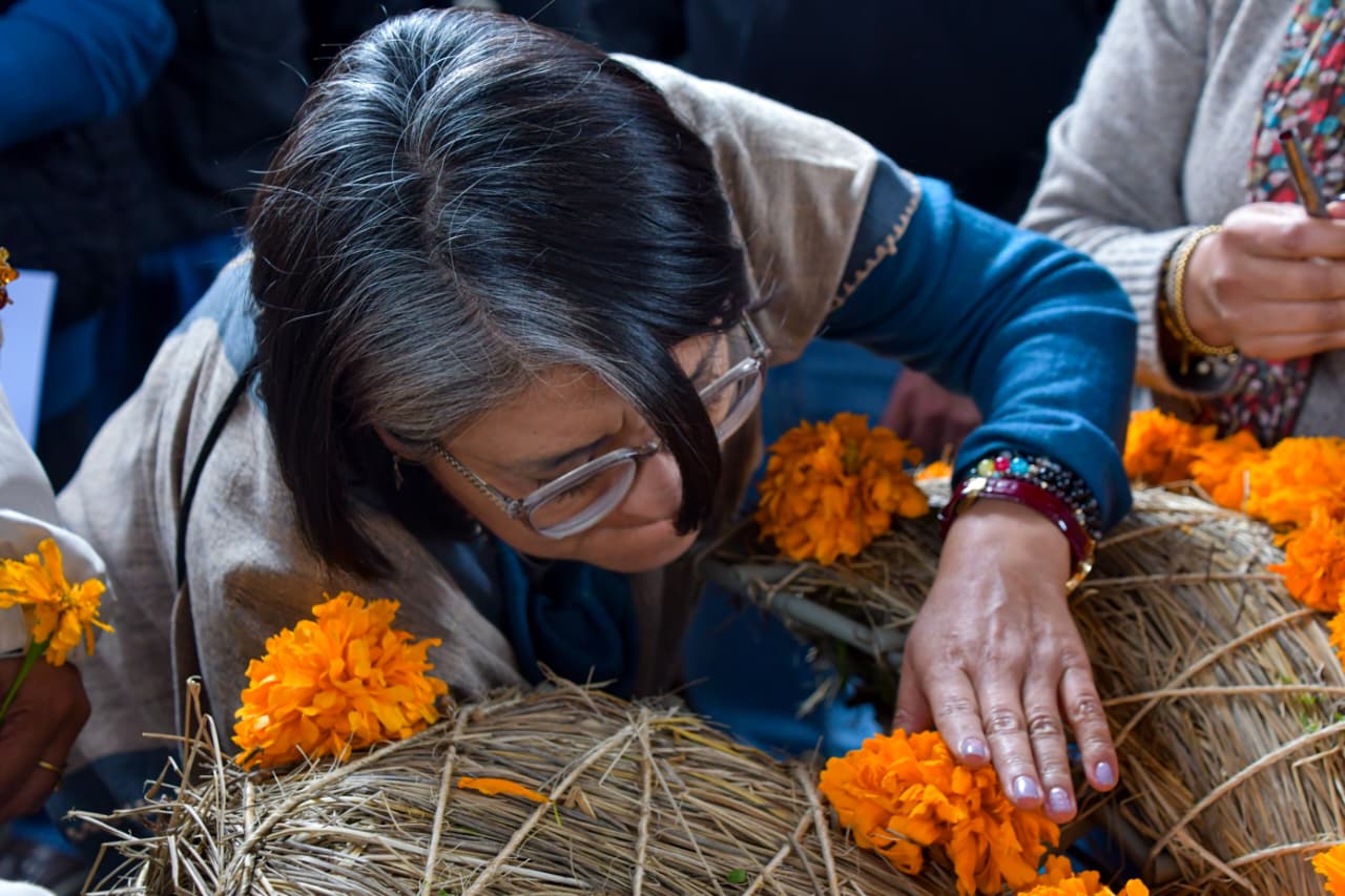 Mujer coloca flores de cempasúchil sobre una estructura de fibras vegetales