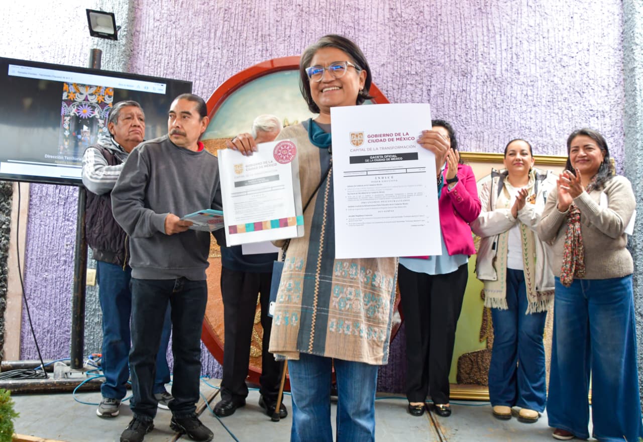 Grupo de vecinos y participantes de una celebración cultural posa con documentos y flores en Iztapalapa