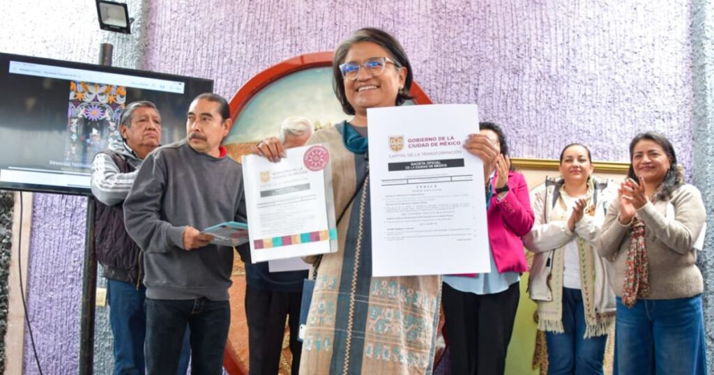 Mujer sostiene dos documentos ante vecinos durante una ceremonia en Iztapalapa