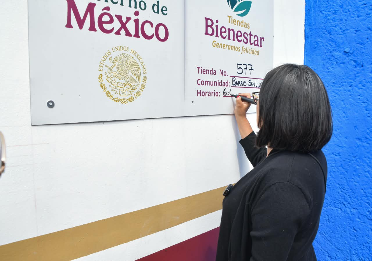 Persona anota información de horario en el letrero exterior de una Tienda Bienestar
