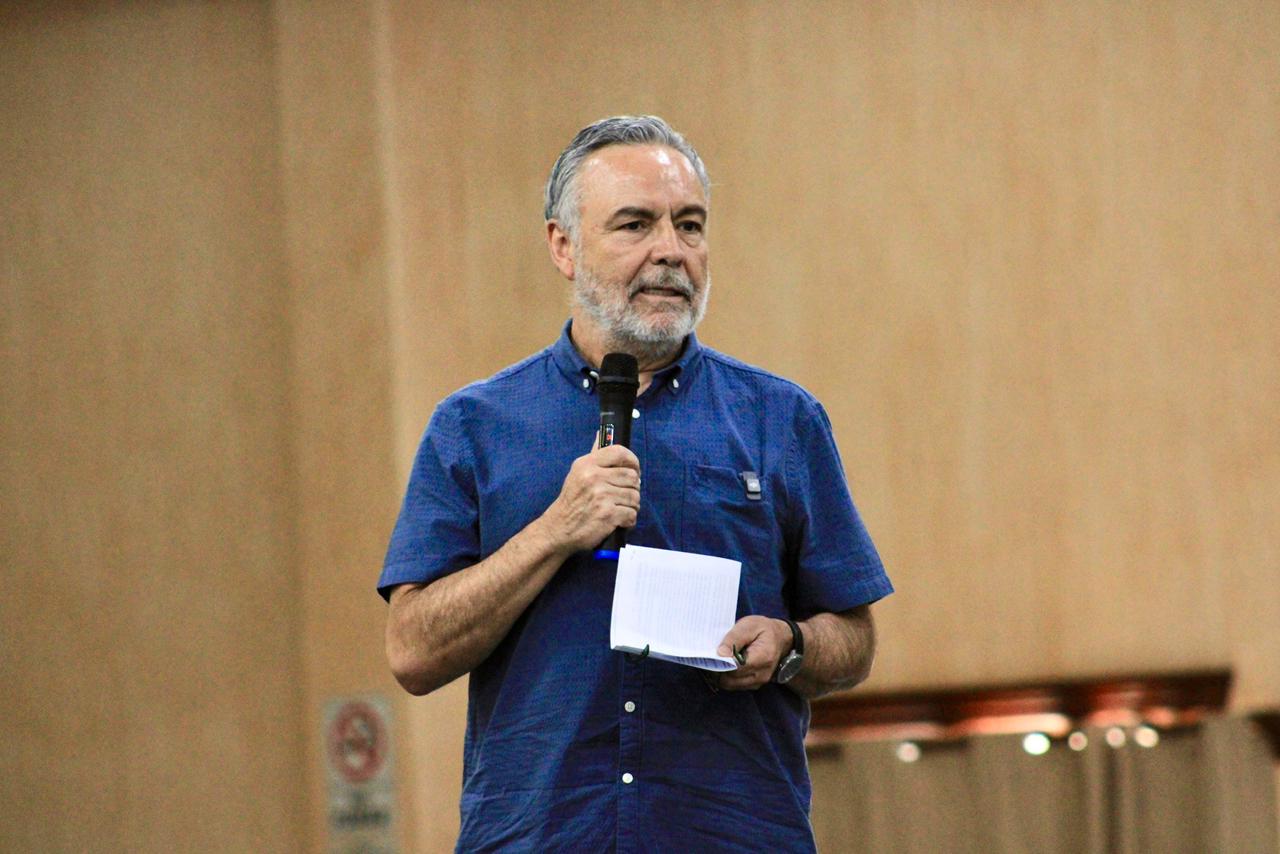 Alfonso Ramírez Cuéllar habla frente a un micrófono y sostiene unas hojas durante un encuentro