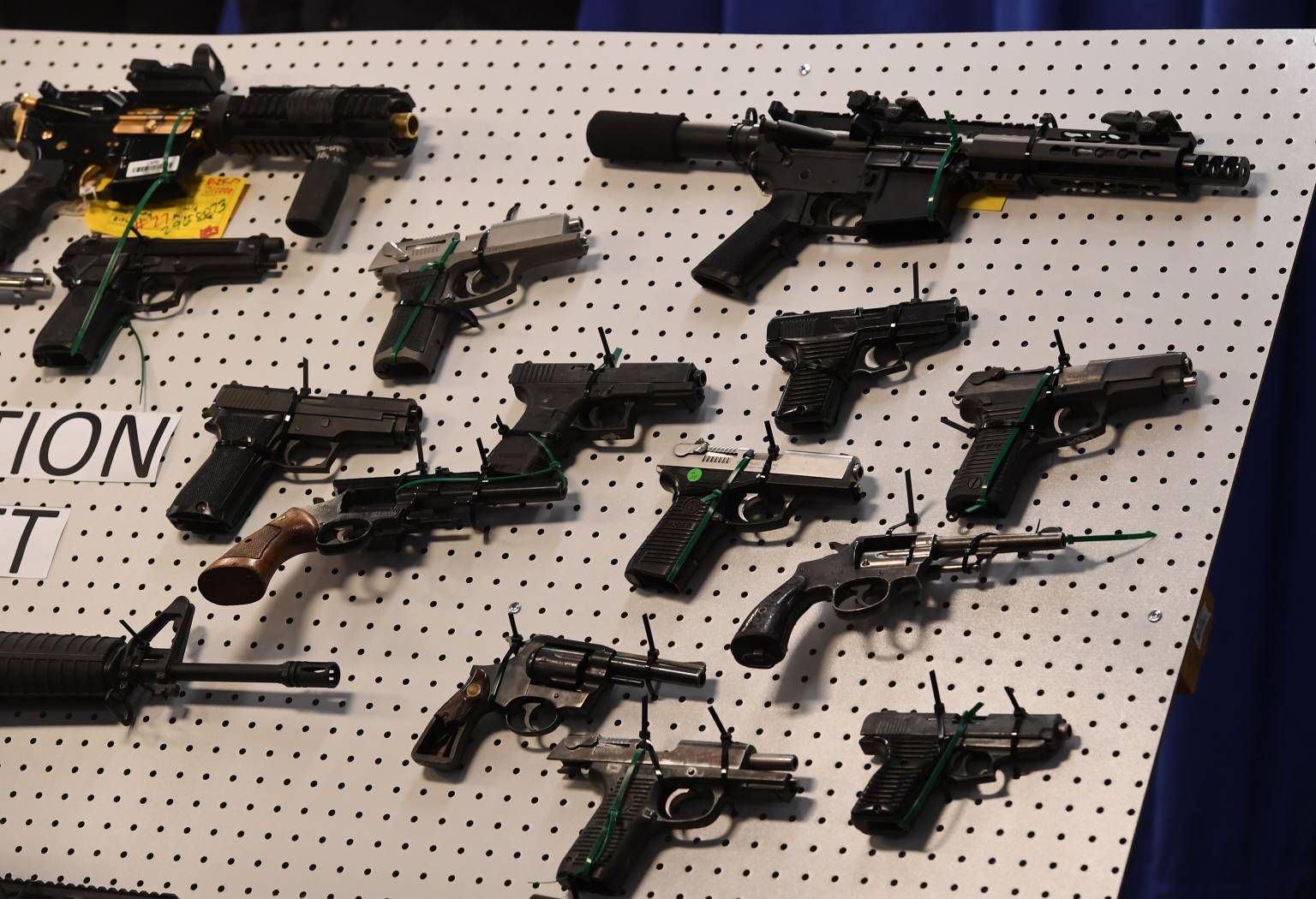 Pistolas, revólveres y rifles sujetos con cinchos a un panel de exhibición