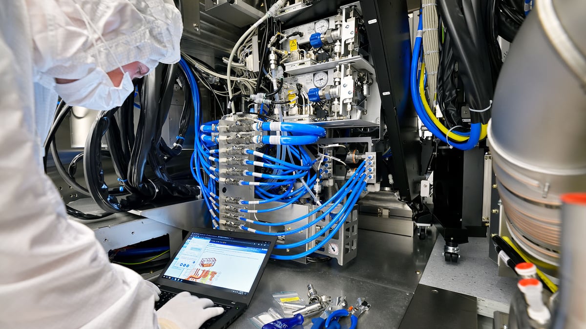 Técnico con traje de protección utiliza un ordenador portátil frente a tuberías y componentes de un equipo industrial especializado