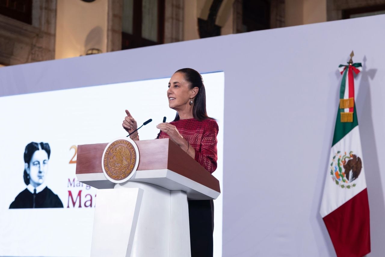Claudia Sheinbaum interviene en una conferencia desde el podio presidencial, junto a la bandera de México.