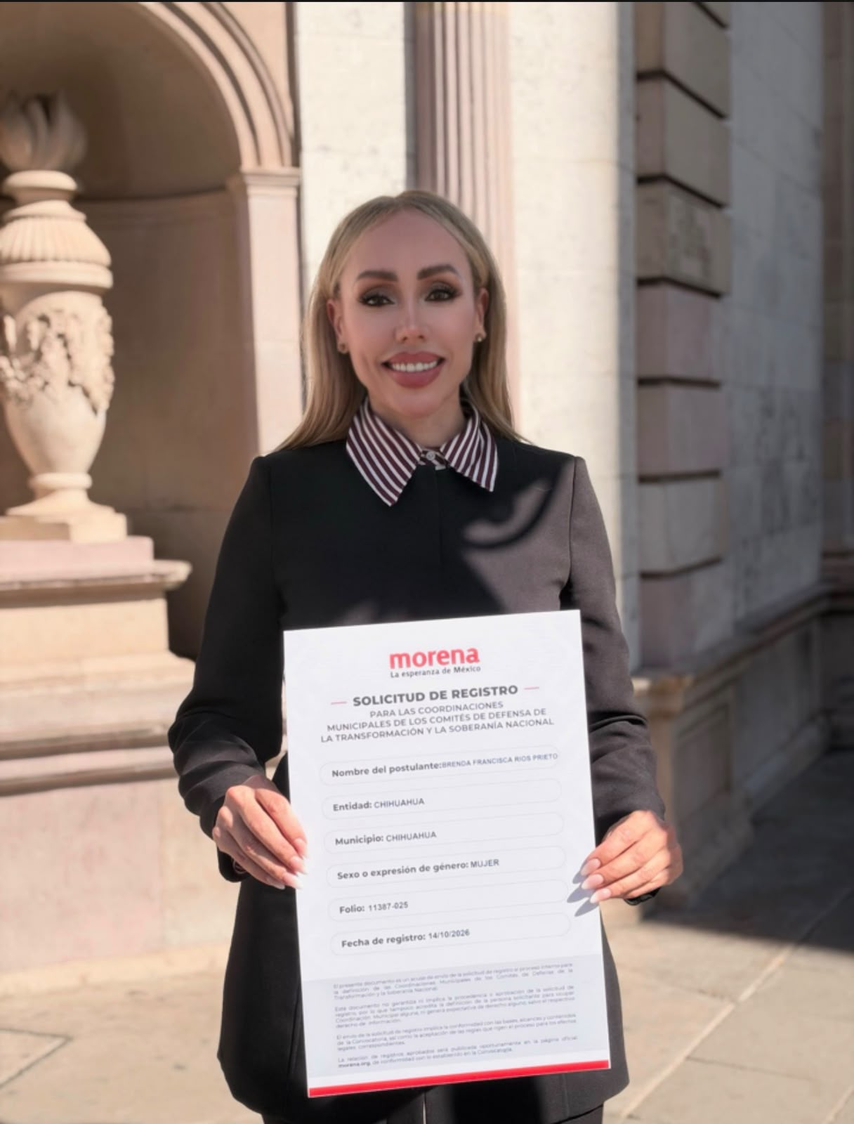 Brenda Ríos sostiene una solicitud de registro de Morena frente a un edificio de piedra.