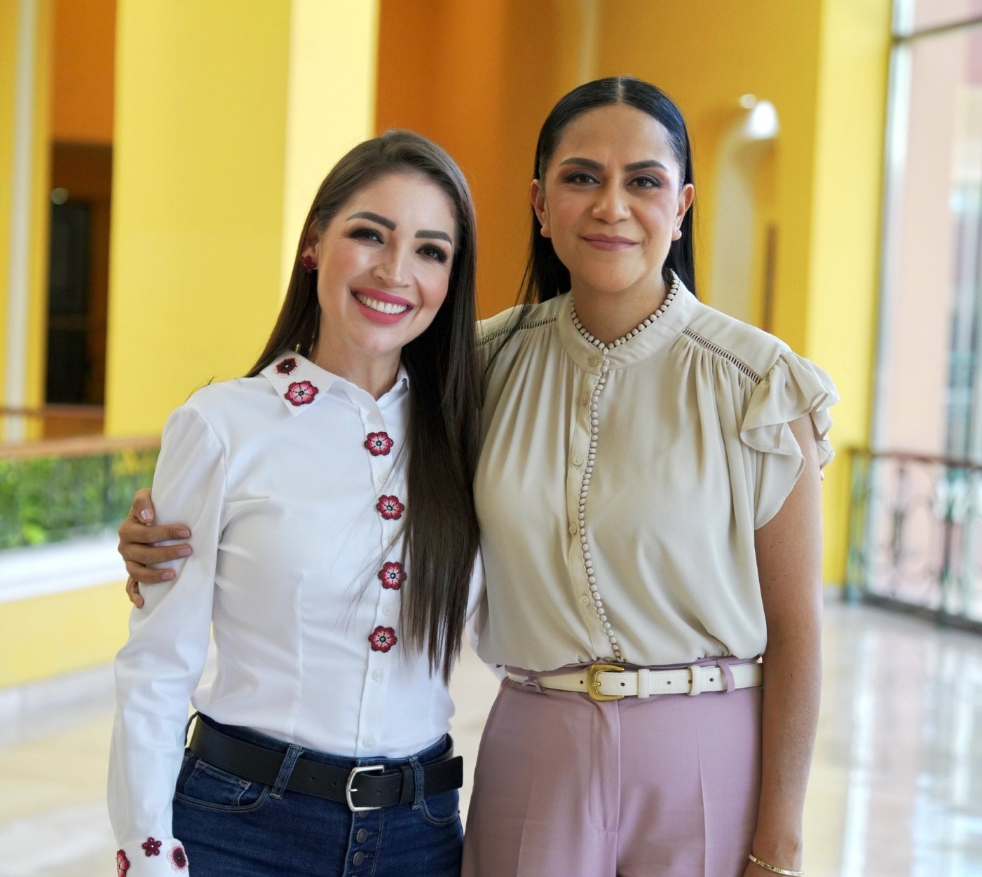 Jasmine Bugarín y Ariadna Montiel posan juntas frente a una pared amarilla, tomadas del hombro