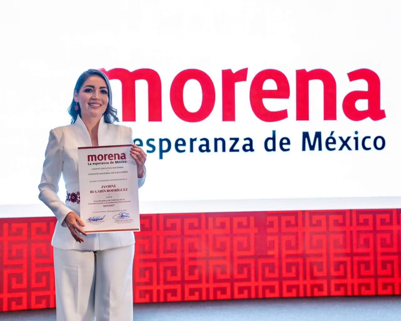 Mujer sostiene una constancia frente a una pantalla con el logotipo de Morena