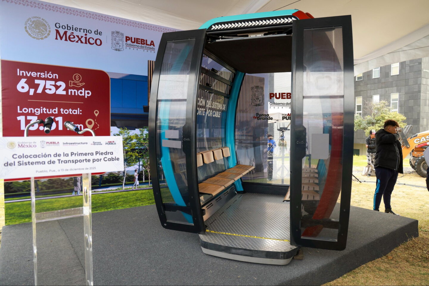 Cabina de muestra del sistema de transporte por cable de Puebla, exhibida junto a un panel de inversión y longitud del proyecto