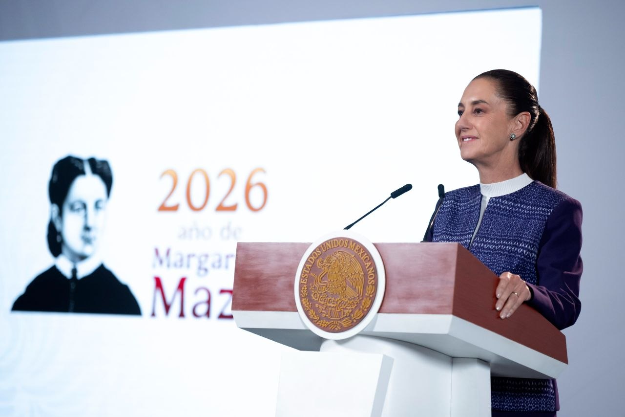 Claudia Sheinbaum detrás de un atril con el escudo nacional y dos micrófonos.