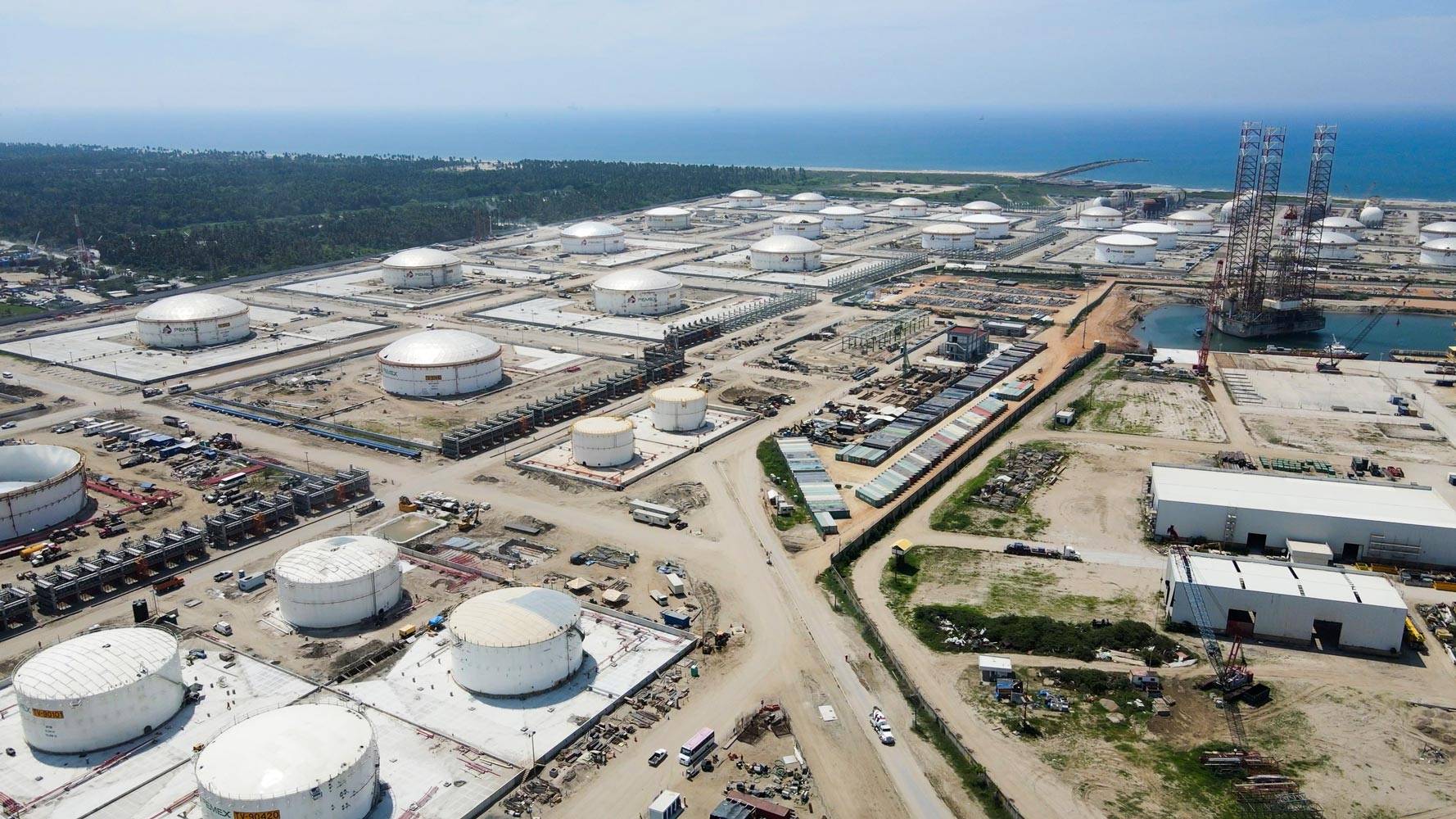 Vista aérea de un complejo industrial costero con numerosos tanques cilíndricos de almacenamiento, tuberías y estructuras