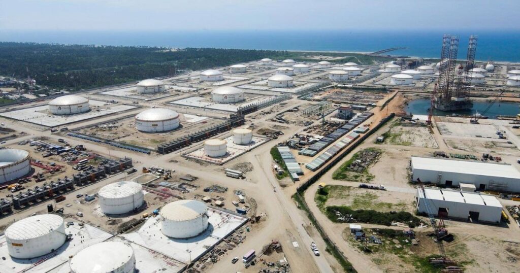 Vista aérea de un complejo industrial costero con numerosos tanques cilíndricos de almacenamiento, tuberías y estructuras