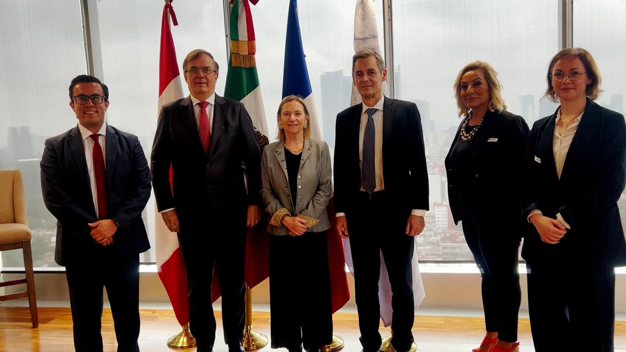 Dos representantes muestran un documento en una reunión con banderas de Canadá y México