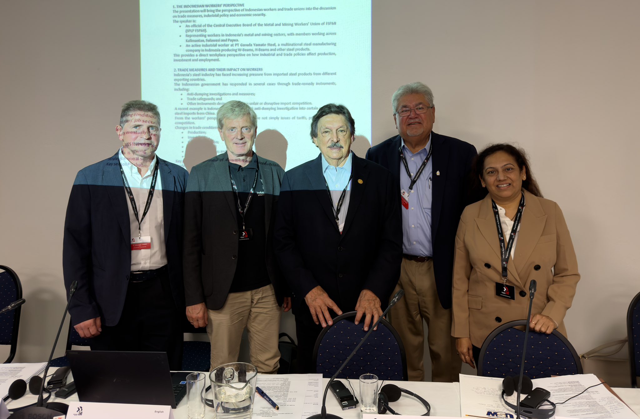 Cinco participantes posan frente a una proyección durante una conferencia sindical internacional