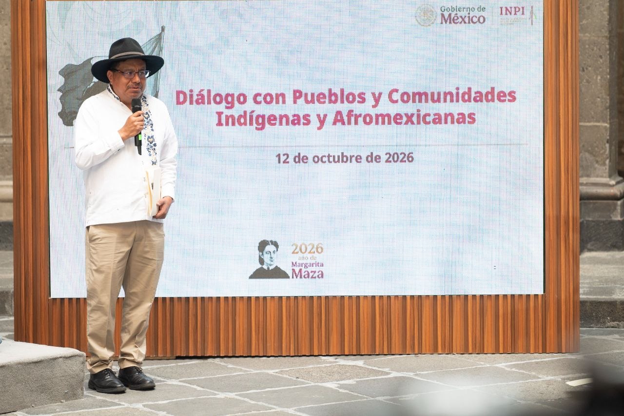 Un hombre con sombrero y camisa blanca habla ante una pantalla que anuncia el Diálogo con Pueblos y Comunidades Indígenas y Afromexicanas del 12 de octubre de 2026.