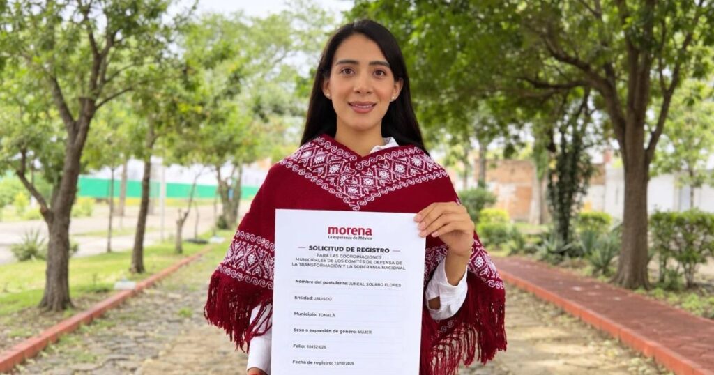Mujer con prenda roja bordada sostiene una solicitud de registro de Morena en un sendero arbolado.