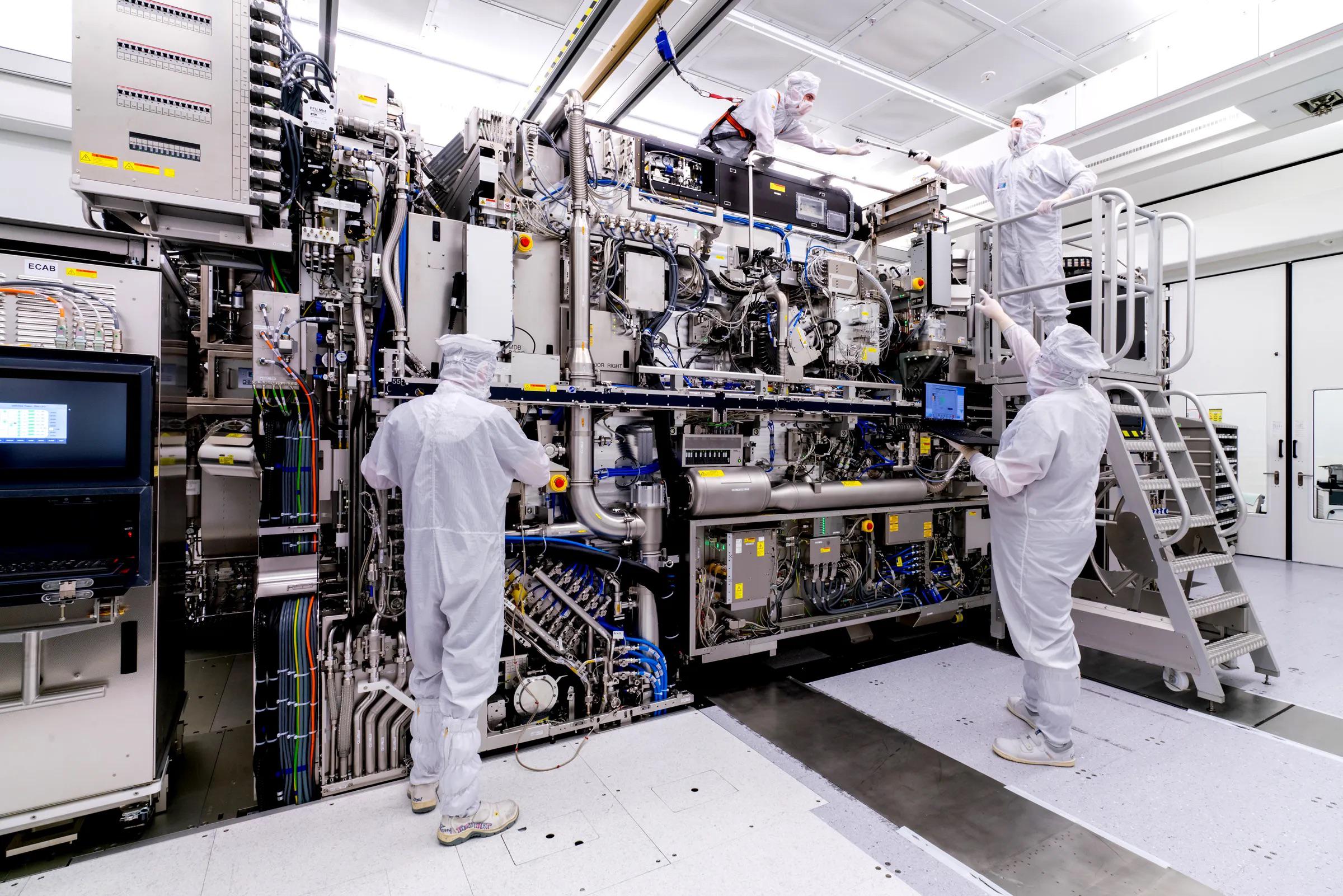 Personal técnico trabaja alrededor de una máquina de litografía de ASML en una sala limpia.