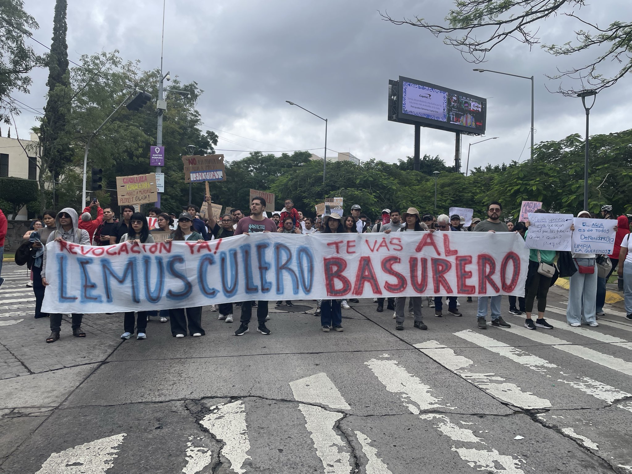 Manifestantes sostienen una manta con las frases «Revocación ya» y «Lemus culero, te vas al basurero» durante una marcha en una avenida de Guadalajara.