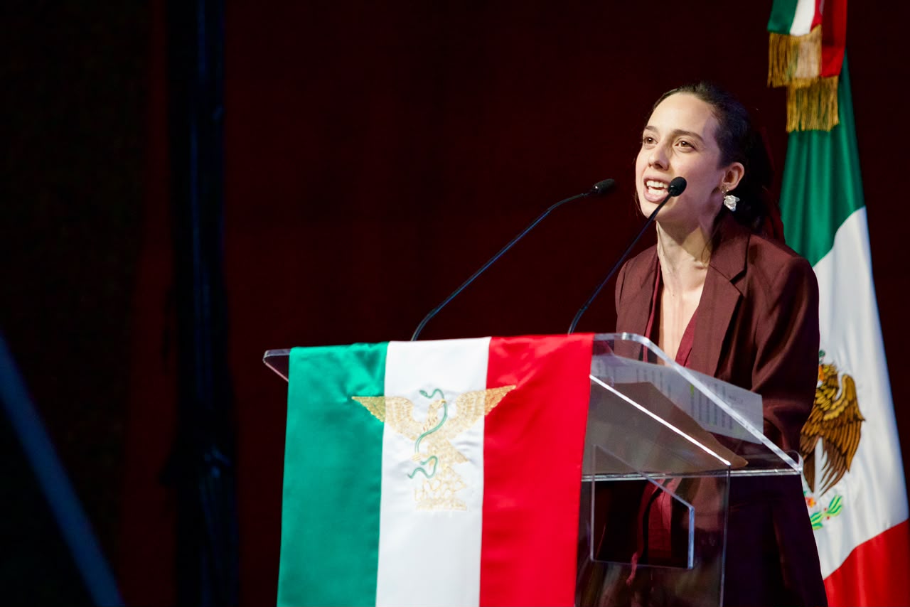Participante del aniversario de Morena ofrece un mensaje desde un podio con la bandera de México.
