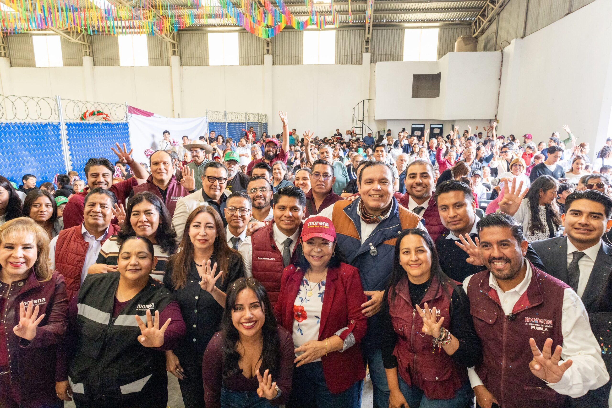 Grupo numeroso de personas posa en un recinto, varias con prendas de Morena y cuatro dedos levantados